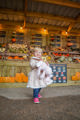 girl stood in front of crates that are filled with pumpkins, gourds and squashes.  