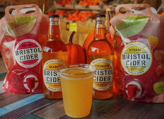 plastic cup of cider, with bristol cider glass bottles in the background. 