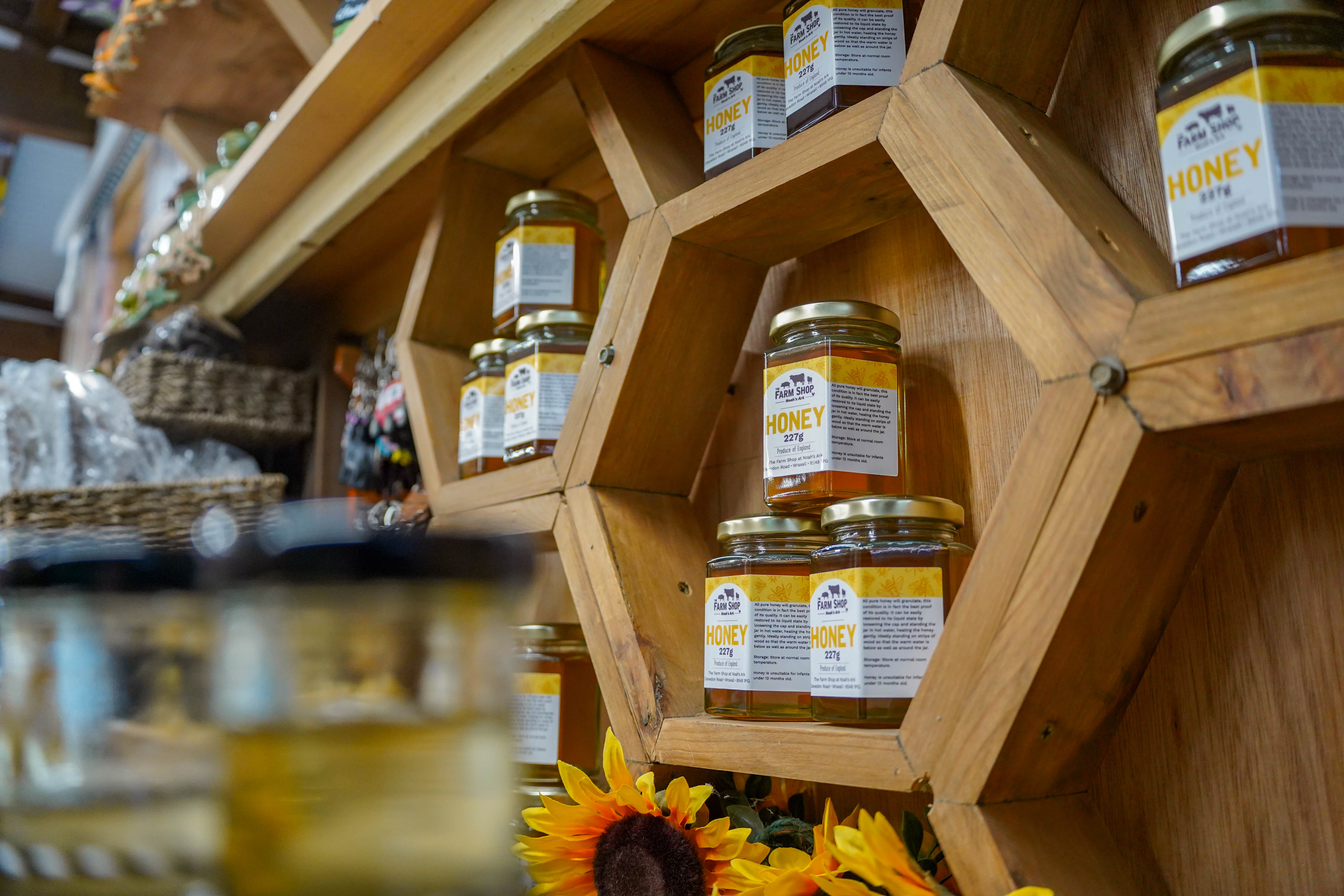 Jars of Farm Shop Honey in stacks of three on honeycomb shaped shelving. 