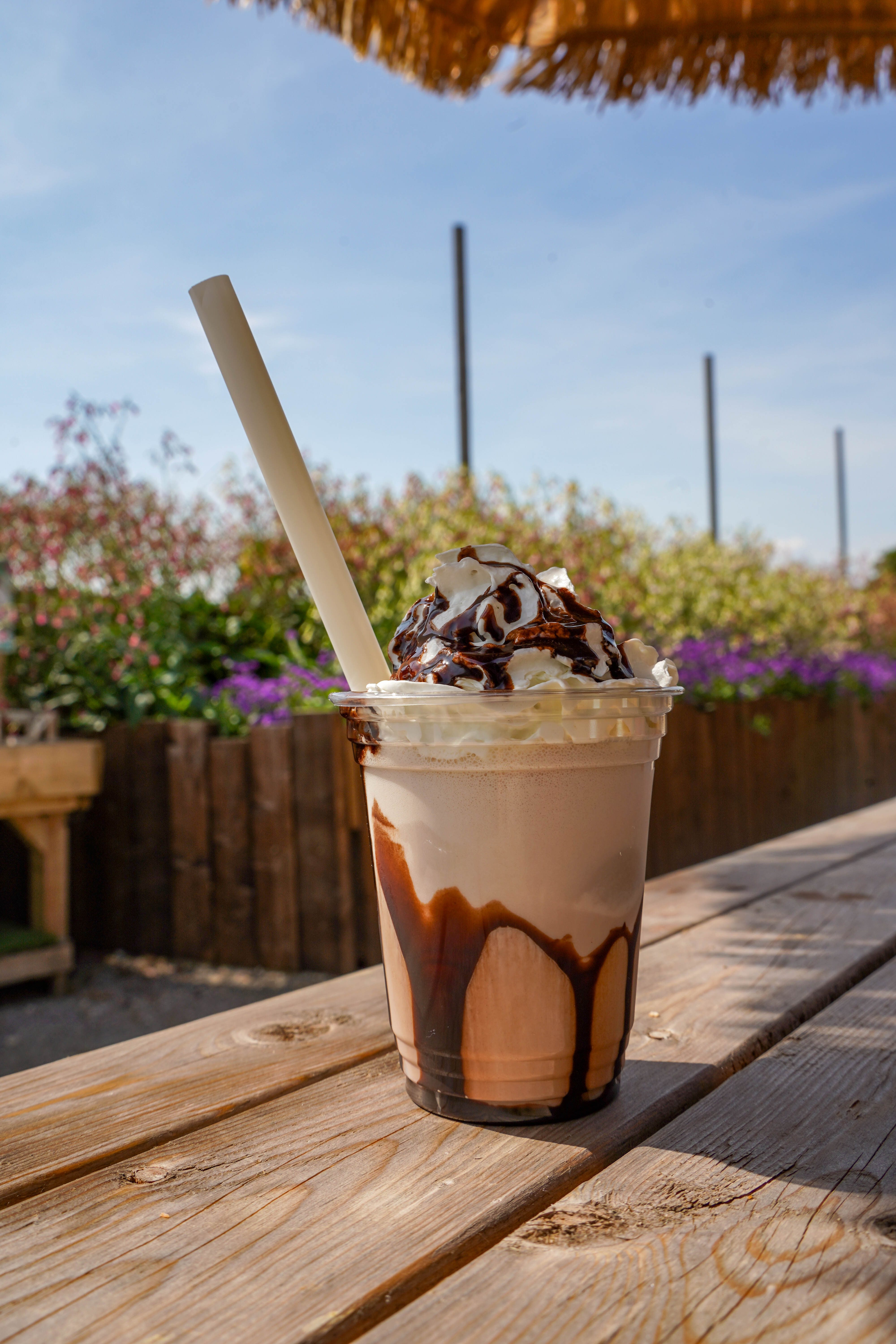 chocolate milkshake with cream and chocolate sauce, on wooden picnic bench outside of farm shop. 
